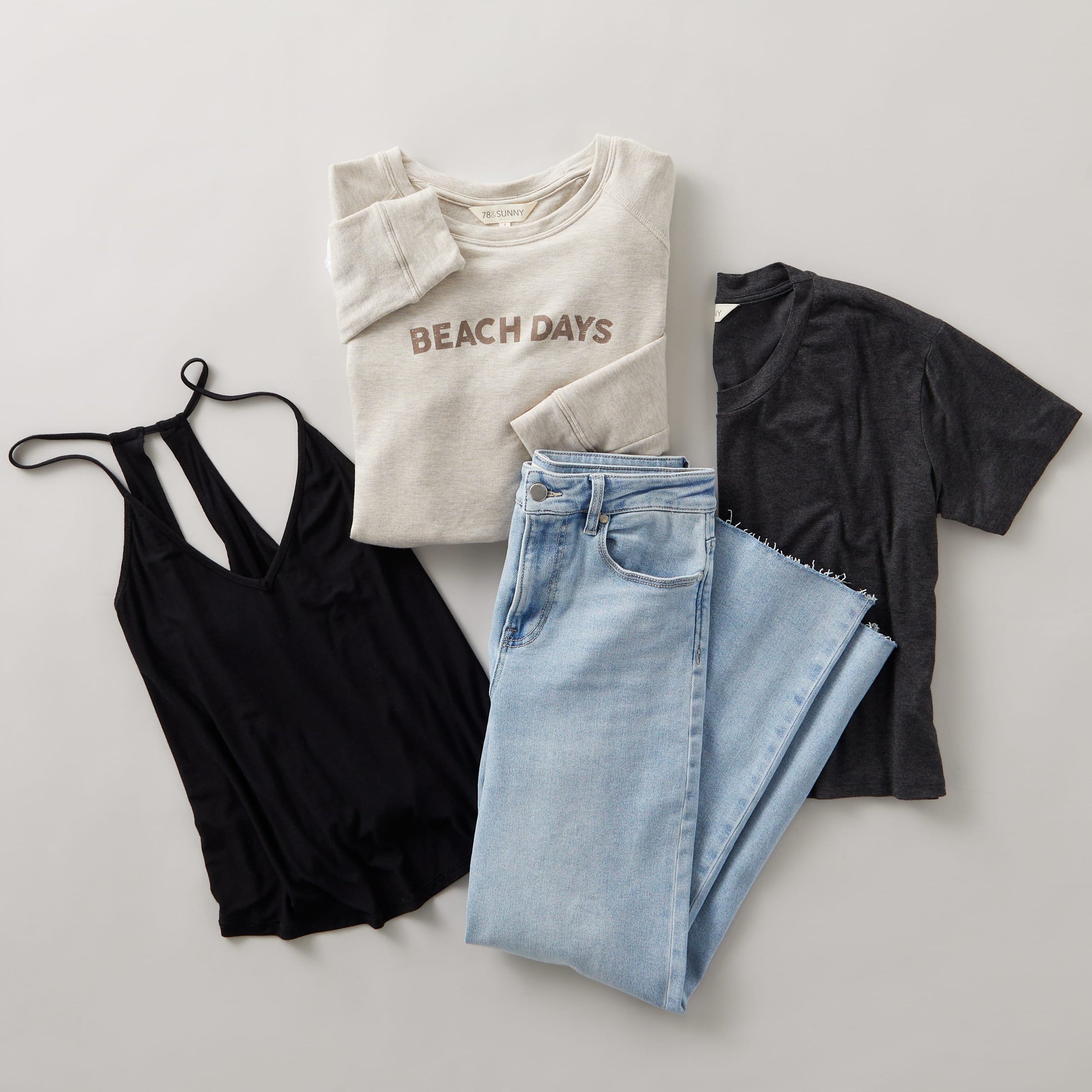 A black tank top, light wash jeans, a tan sweatshirt and a tee shirt laying stacked on a white background.