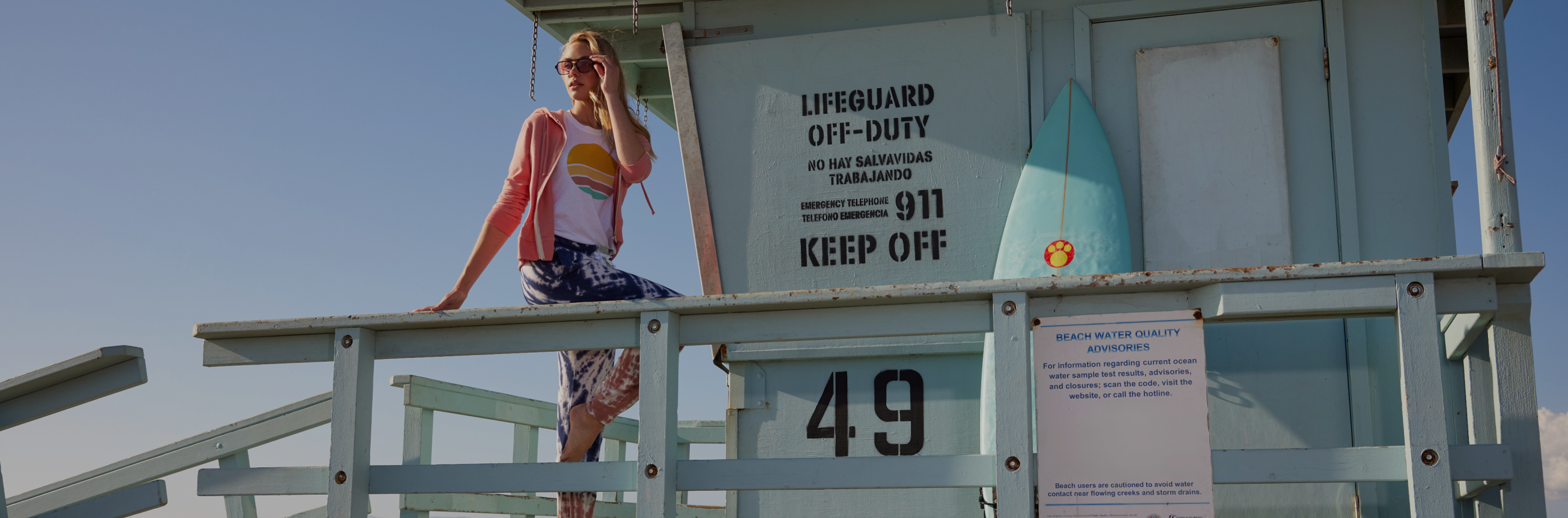 A 78&Sunny model leaning on the railing of a lifeguard stand with her hand up to her face. 